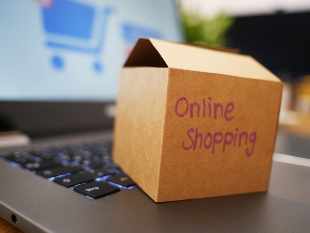Das Bild zeigt einen kleinen Karton, auf dem Online Shopping steht. Der Karton ist sehr klein und liegt auf einem Laptop.